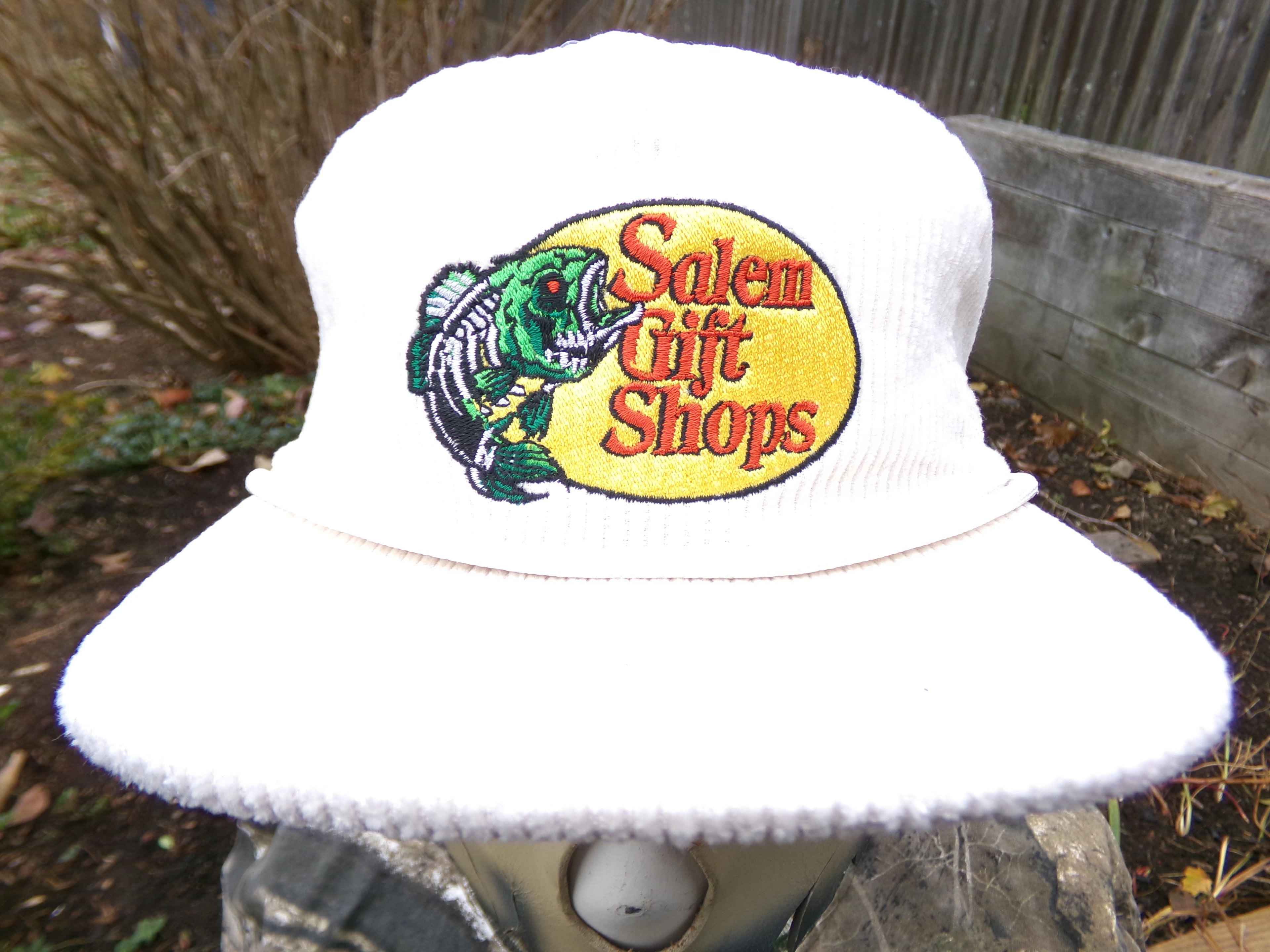 White bucket hat with 'Salem Gift Shops' logo on a blurred outdoor background