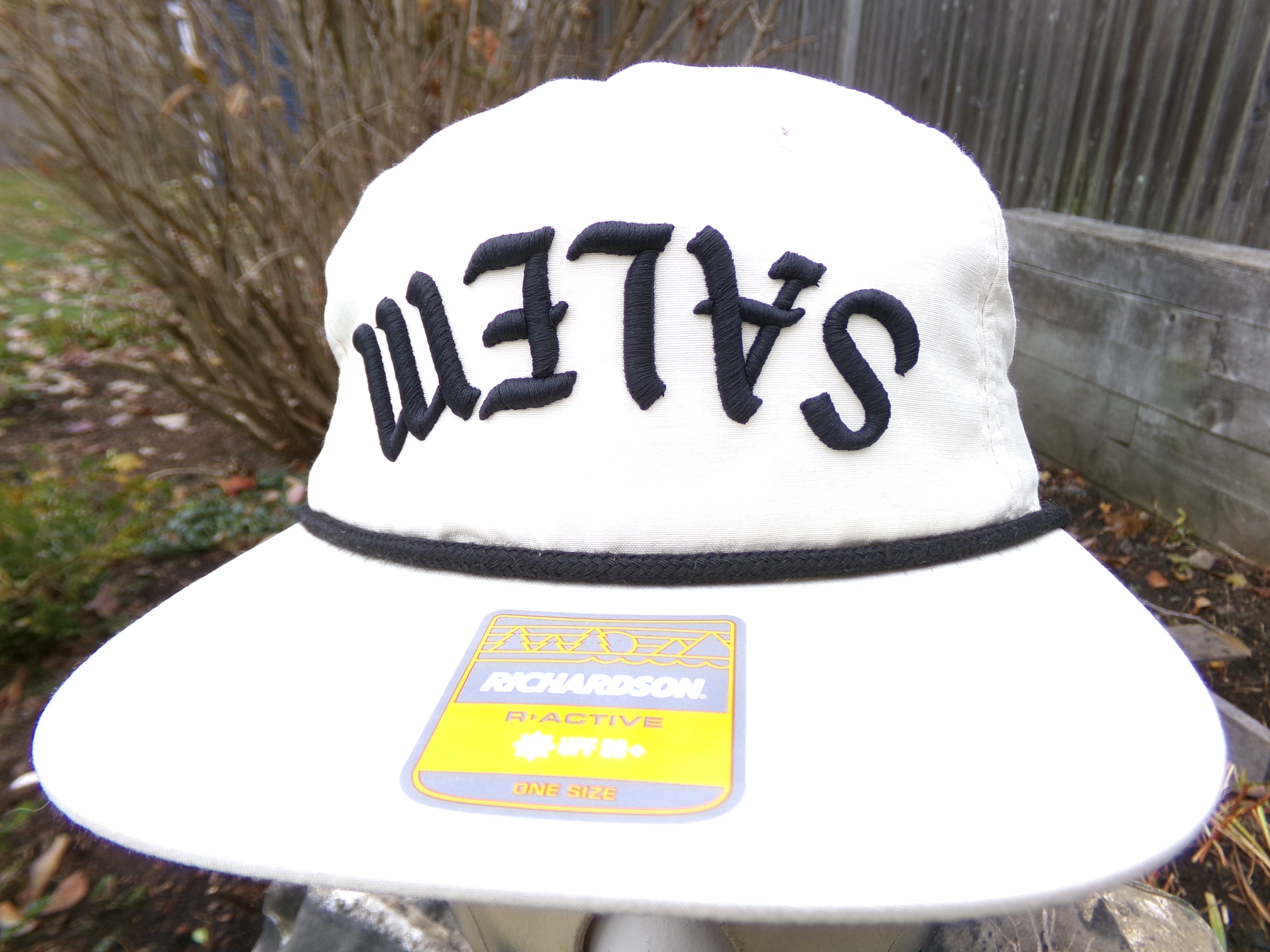 White cap with 'SALEM' text on a blurred outdoor background