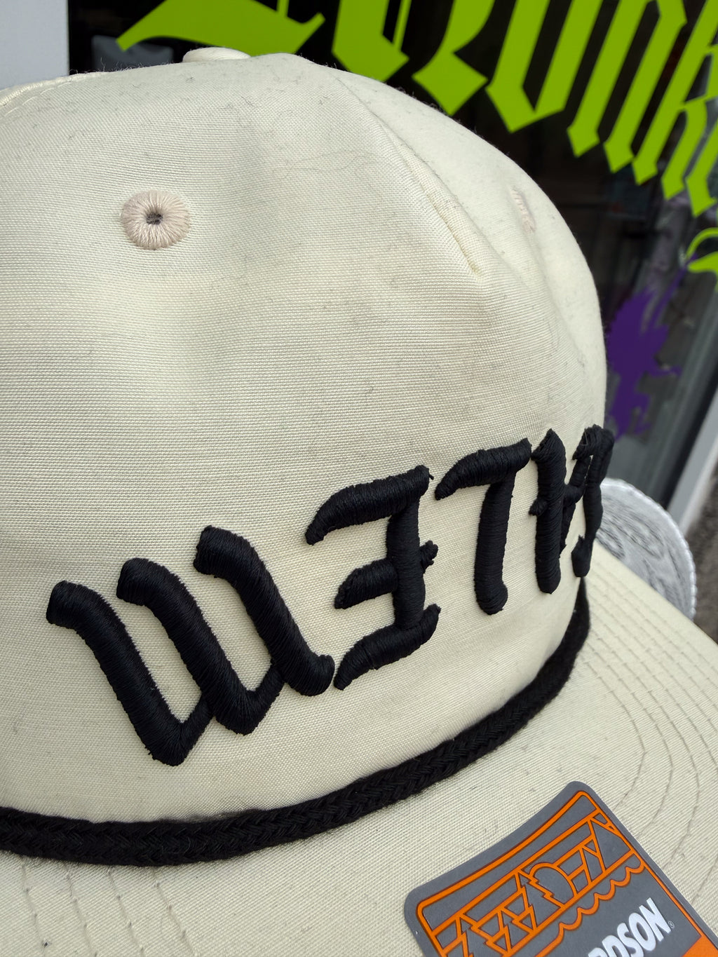 Beige cap with black embroidered text and a logo patch on a blurred background