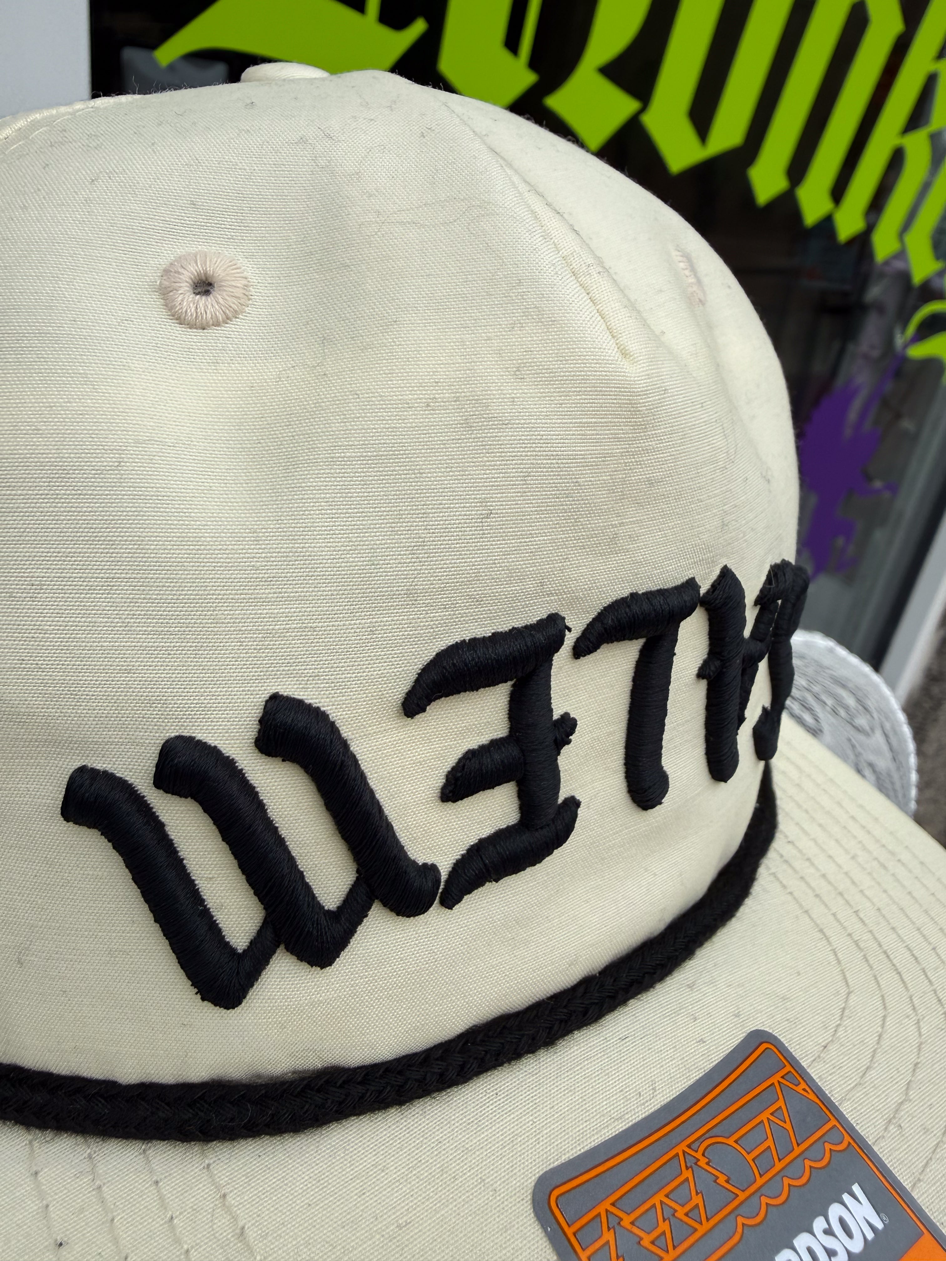 Beige cap with black embroidered text and a logo patch on a blurred background