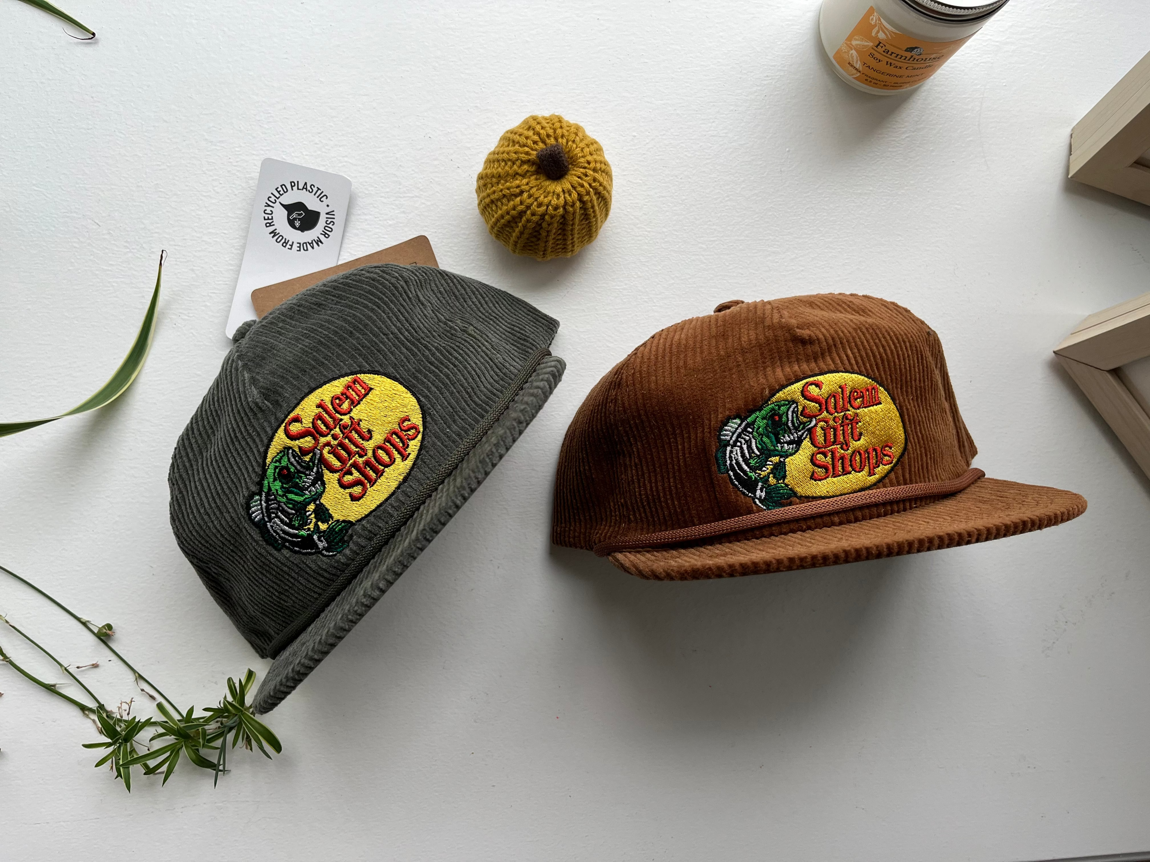 Two hats, one green and one brown, with embroidered logos on a white surface.